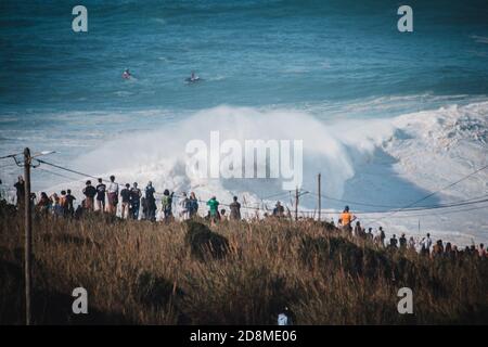 Menge auf Klippe am North Beach Wellen beeindruckende Welle und Wellen von mutigen Surfern, Portugal Stockfoto