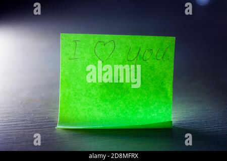 Ich liebe Sie Nachricht auf hellem grünen Blatt Schreibpapier Notiz mit Herz auf blauem Hintergrund geschrieben. Stockfoto