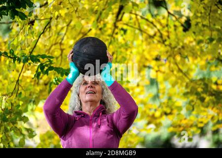 Eine Frau in den Sechzigern, die im Herbst Gewichte im Freien hebt. Stockfoto