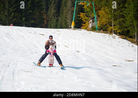Glücklicher Vater lehrt Tochter Skifahren, während sie zwischen seinen Beinen halten. Stockfoto