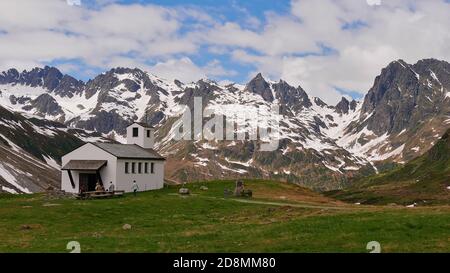 Wanderer ruhen auf Bänken vor einer kleinen Kapelle in der Nähe von Silvretta Stausee, Montafon, Österreich mit herrlichem Bergpanorama im Hintergrund. Stockfoto