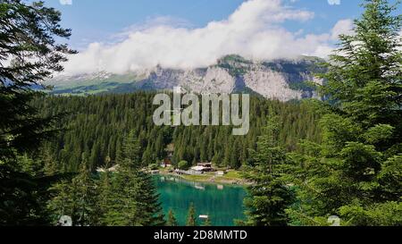 Türkisfarbener Caumasee umgeben von Wald im Wasser bei Flims, Graubünden, Schweiz mit Standseilbahn, Restaurant und Bergen. Stockfoto