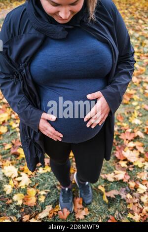 Glückliche Zukunft schwangere Frau Blick auf ihren Bauch von oben Und den Bauch mit den Händen im Park halten Der Herbst mit einem Bündel von bunten Stockfoto