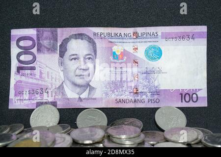 100 Philippinischer Peso-Papierbrief über einem Haufen Peso Münzen Stockfoto