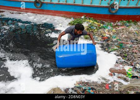 Dhaka, Bangladesch. Oktober 2020. Ein Mann aus Bangladesch wäscht leere Plastikfässer, die zum Transport von Chemikalien verwendet wurden, im Wasser des Buriganga River, bevor er sie recycelt, in Dhaka, Bangladesch, 31. Oktober 2020. Die chemischen Abfälle von Mühlen und Fabriken, Hausmüll schließlich seinen Weg in den Buriganga Fluss, der als Dhakas Lebensader gilt. Tausende von Menschen sind täglich auf den Fluss angewiesen, um zu baden, Kleidung zu waschen, Lebensmittel zu bewässern und Waren zu transportieren. Der Fluss hat einen extremen Verlust an Biodiversität erlitten und ist nun schwarz geworden. (Bild: © Suvra Kanti Da Stockfoto