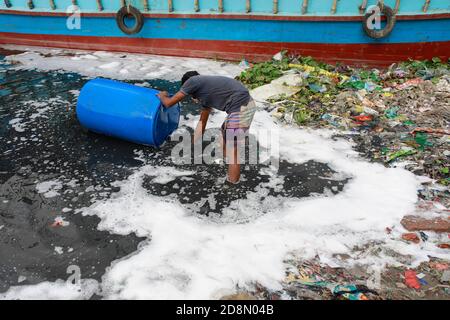 Dhaka, Bangladesch. Oktober 2020. Ein Mann aus Bangladesch wäscht leere Plastikfässer, die zum Transport von Chemikalien verwendet wurden, im Wasser des Buriganga River, bevor er sie recycelt, in Dhaka, Bangladesch, 31. Oktober 2020. Die chemischen Abfälle von Mühlen und Fabriken, Hausmüll schließlich seinen Weg in den Buriganga Fluss, der als Dhakas Lebensader gilt. Tausende von Menschen sind täglich auf den Fluss angewiesen, um zu baden, Kleidung zu waschen, Lebensmittel zu bewässern und Waren zu transportieren. Der Fluss hat einen extremen Verlust an Biodiversität erlitten und ist nun schwarz geworden. (Bild: © Suvra Kanti Da Stockfoto