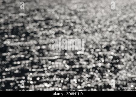 3 - abgestuftes Licht zu dunklem Bokeh, gebildet aus Wasserwellen und Sonnenlicht, was einen abstrakten strukturierten monochromen Hintergrund, schwarz und weiß. Stockfoto