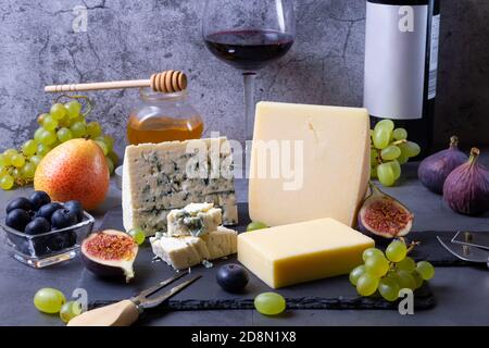 Blauer Käse und Parmesan auf einem schwarzen Brett, Obst, Wein und Honig. Nahaufnahme. Stockfoto