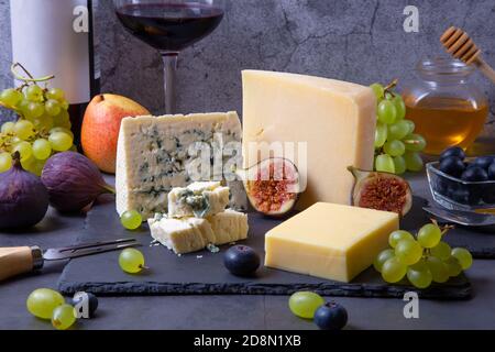 Blauer Käse und Parmesan auf einem schwarzen Brett, Obst, Wein und Honig. Nahaufnahme. Stockfoto