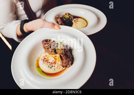 Der Kellner hält einen Teller Leckere saftige Fleisch Schnitzel, Kartoffelpüree bestreut mit grünen und frischen gesunden Salat von Tomaten und Kopfsalat Stockfoto