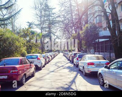Russland, Sotschi 18.02.2020. Autos werden auf einer schmalen Straße entlang der Straße mit Bäumen neben dem Wohnhaus geparkt Stockfoto