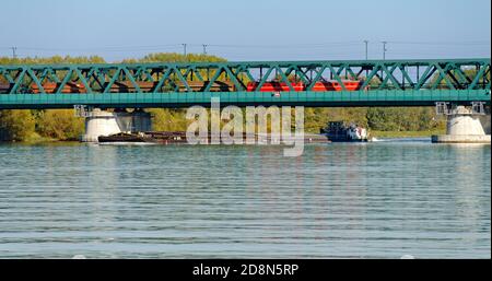 Frachtschiff unter einer Brücke mit überfahrenden Güterzug auf der Donau bei der Stadt Tulln, Österreich Stockfoto