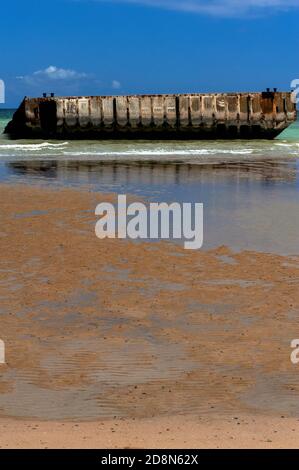 Bei Ebbe in Arromanches, Calvados, Normandie, Frankreich, Die Menschen können zu Fuß an den Rand des Wassers auf dem Zweiten Weltkrieg ‘Gold Beach’ zu erreichen - aber nicht betreten - vorgegossene Betonabschnitte von Port Winston oder Mulberry Harbour B. Dies war der 600,000-Tonnen-vorgefertigte tragbare Hafen, der über den Ärmelkanal geschleppt wurde, Vor der Küste montiert und dann für 10 Monate nach der Operation Overlord ‘D-Day’ Invasion vom 6. Juni 1944 verwendet, um 2.5 Millionen britische und kanadische Truppen, eine halbe Million Fahrzeuge und vier Millionen Tonnen Vorräte zu landen. Stockfoto