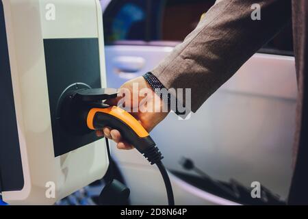 Farbbild der Hand eines Mannes, die Vorbereitung auf ein Elektroauto aufladen. Stockfoto