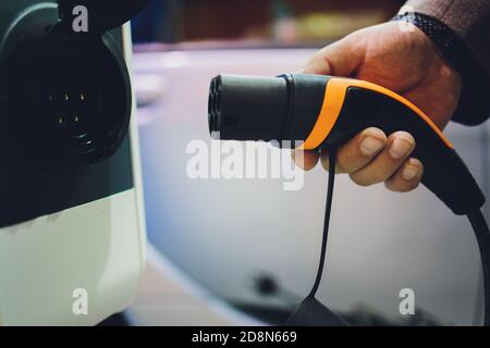 Farbbild der Hand eines Mannes, die Vorbereitung auf ein Elektroauto aufladen. Stockfoto