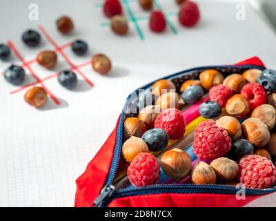 Zurück zur Schule Konzept. TIC-tac-toe Logik-Spiele von Himbeeren, Heidelbeeren und Haselnüsse in quadratischen Notizbuch in der Nähe Bleistifttasche mit Beeren verpackt. Stockfoto