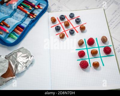 Leckere Schulferien und lustige Spiele in der Schule. TIC-tac-toe von Himbeeren, Heidelbeeren und Haselnüssen. Stiftetui mit Buntstiften und Schokolade. Stockfoto