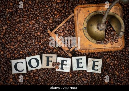 Draufsicht auf eine alte manuelle Kaffeemühle mit gerösteten Kaffeebohnen und dem Text Kaffee aus Holzblöcken. Stockfoto