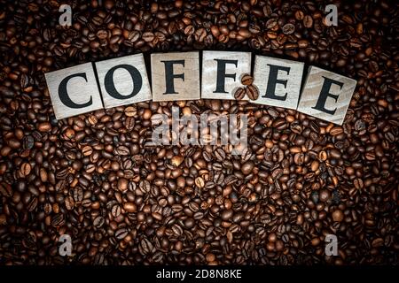 Einzelwort Kaffee, aus Holzblöcken auf Hintergrund mit gerösteten Kaffeebohnen. Stockfoto