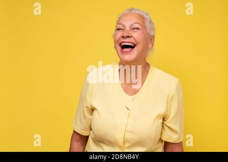Ältere Frau lächelt glücklich lachend an der Kamera an der gelben Wand. Stockfoto