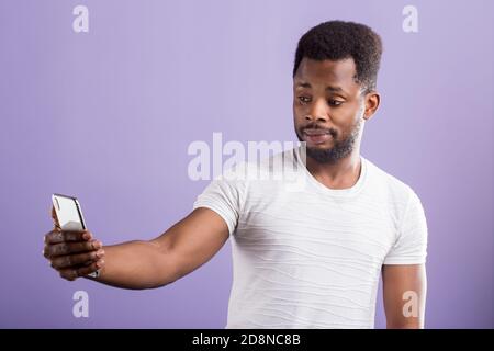 Foto von stauned verwirrt schwarzen Mann hält moderne Handy, Selfie. Reaktion, Technologie, Gesichtsausdrücke Konzept. Stockfoto