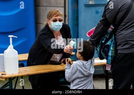 Eine Frau, die eine Gesichtsmask trägt, nimmt die Temperatur eines Jungen auf, der in einen Fußballplatz kommt. Stockfoto