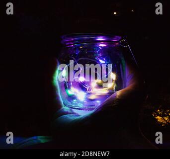 Hand hält Maurer Jar mit Neon-LED-Leuchten im Inneren gefüllt. Stockfoto