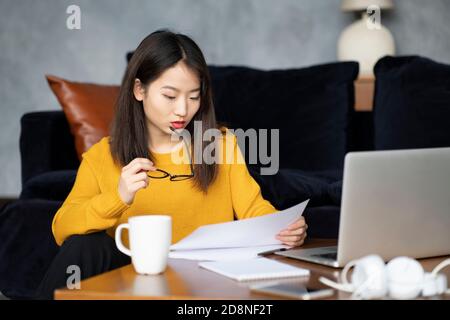Asiatische Frau, die zu Hause arbeitet und Dokumente ansieht. Schöne japanische Freiberuflerin Stockfoto