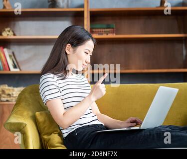 Asiatische Frau Finger wagging Blick auf Laptop, Arbeit zu Hause, Liying auf dem Sofa Stockfoto
