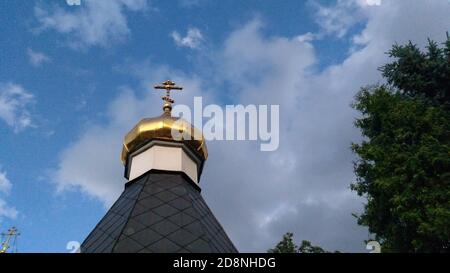 Das goldene Kreuz auf der Spitze der russisch-orthodoxen Kirche bei Die Altstadt unter blauem Himmel mit flauschigen Wolken Stockfoto