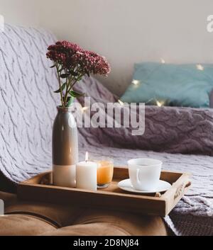 Eine Tasse Tee auf einem Holztablett, brennende Kerzen, ein Blumenstrauß Stockfoto
