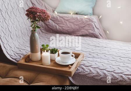 Eine Tasse Tee auf einem Holztablett, brennende Kerzen, ein Blumenstrauß Stockfoto
