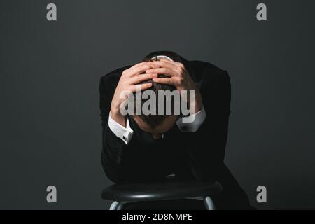 Studioportrait eines jungen kaukasischen Mannes im Smoking, Hände im Haar, traurig nach unten schauend, vor schlichtem Studiohintergrund Stockfoto