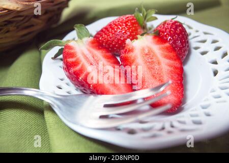 Detail von einigen Erdbeeren auf einer Untertasse, einer von ihnen ist in der Hälfte geschnitten und die Struktur des Behälters ist hervorgehoben Stockfoto