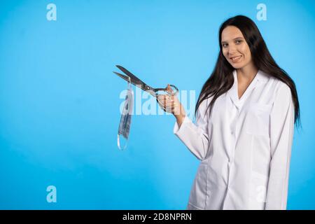 Eine junge Ärztin will die Pandemie beenden und diese beunruhigende Zeit beenden, indem sie symbolisch den Gummi der Schutzmaske schneidet. Stockfoto