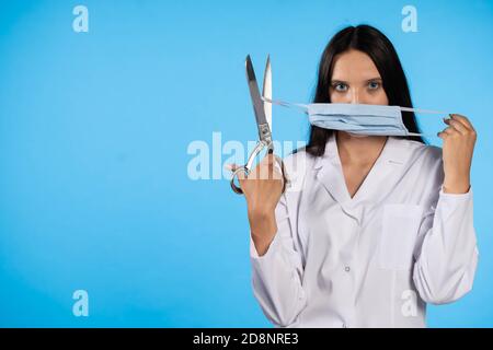 Eine junge Ärztin will die Pandemie beenden und diese beunruhigende Zeit beenden, indem sie symbolisch den Gummi der Schutzmaske schneidet. Stockfoto