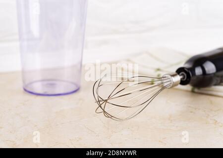 Nahaufnahme des Stabmixers zum Schlagsahne und Tasse auf einem Tisch. Moderne elektrische Küchengeräte für die Herstellung von Saucen, Smoothies, Püree. Stockfoto