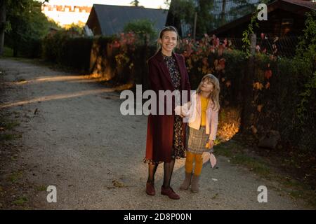 Familie, Saison und Menschen Konzept - glückliche Mutter und kleine Tochter zu Fuß entlang Herbst Park an der Straße im Dorf. Das Spiel von Licht und Stockfoto