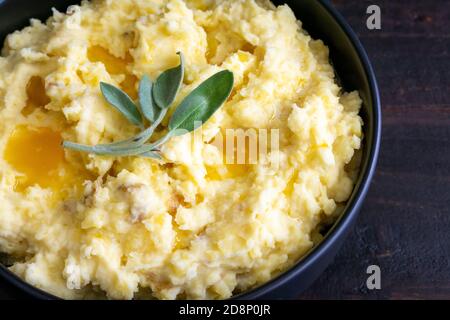 Kartoffelpüree mit Butter- und Salbblättern: Pürierte Yukon-Goldkartoffeln mit Schalen mit geschmolzener Butter und einem Zweig frischer Kräuter Stockfoto