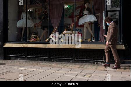 Ein Mann mit Anzug und OP-Maske geht am Moschino-Laden in der Conduit Street, London, England vorbei Stockfoto