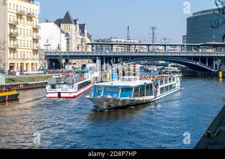 Ausflugsboote mit Menschen auf der Spree in Berlin Mit der Eisenbahnbrücke und anderen Gebäuden im Hintergrund Stockfoto