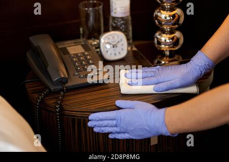 Zugeschnittenes Foto von Mädchen tragen Schutzhandschuhe und wischen Möbel mit einem Lappen. Servicekonzept des Hotels Stockfoto