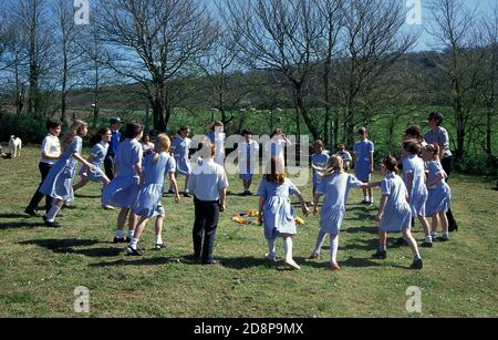 Grundschulkinder machen einen traditionellen englischen Landtanz in Offenes Feld um einen Blumenkreis Stockfoto