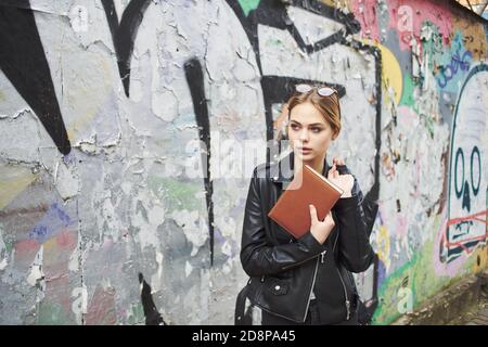 Frau in Lederjacke in der Nähe Graffiti an der Wand in Die Straße Stockfoto