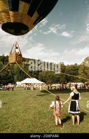 Heißluftballonfahrer aus Atlanta testet sein Handwerk im Tethered Flight im Helen Valley; Ort des fünften jährlichen Oktoberfestes in Helen. Das hintere Zelt diente als Hauptquartier für das Festival die Mutter und Tochter in bayrischer Kleidung waren unter vielen Besuchern, die sich für eine Chance auf einen kostenlosen Tethered-Flug im Ballon anstellten. Die Stadt begann mit dem Oktoberfest, nachdem sie ihr Geschäftsviertel mit alpinem Thema renoviert hatte Stockfoto