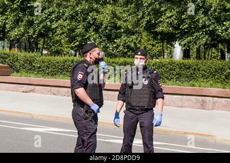 Zwei bewaffnete Bodyguards in schwarzen Uniformen, Schutzmasken, Handschuhe patrouillieren Stadtstraßen während der globalen Pandemie. Stockfoto