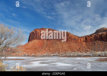 Traditionelle Südwestlandschaft mit roten Sandsteinbergen mit gefrorenem Fluss im Vordergrund und blauem Himmel mit Wolken. USA, Arizona, Utah. Stockfoto