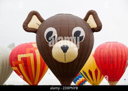 Ein süßes Teddybär Gesicht auf einem Heißluftballon umgeben von anderen bunten Ballons mit einem weißen bewölkten Himmel auf der Balloon Fiesta in New Mexico. Stockfoto