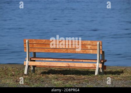 Eine einzige leere Holzbank mit Blick auf ein ruhiges blaues Meer Stockfoto