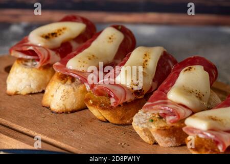 Tapas mit Iberico-Schinken, Mozzarella-Käse, geröstete Paprika auf einer Scheibe geröstetem Baguette mit Olivenöl, Petersilie und Knoblauch Stockfoto